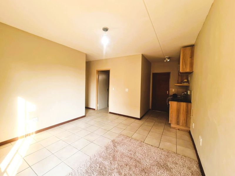 An open-plan living area featuring tiled flooring and a compact kitchenette with built-in cabinetry and dark countertops.