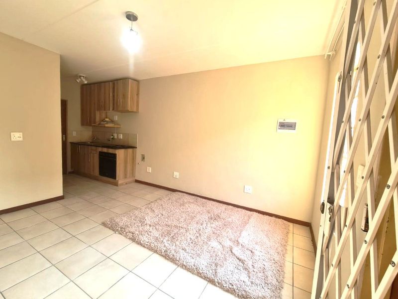 Open-plan living area featuring tiled flooring and a compact kitchen with built-in cabinetry, oven, and hob, leading to a secure entrance.