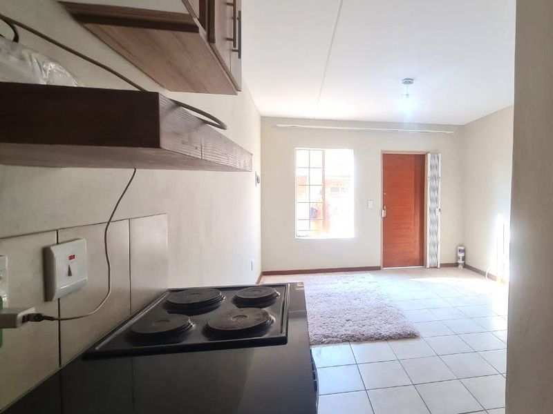 Open plan kitchen and living area featuring tiled flooring, built-in cabinetry, and an electric hob, leading to an exterior door.
