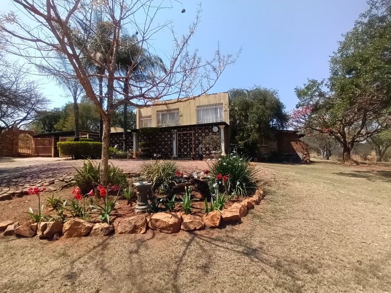 Front view of the farm property featuring a paved driveway, established garden with stone edging, and a covered patio area with security bars.