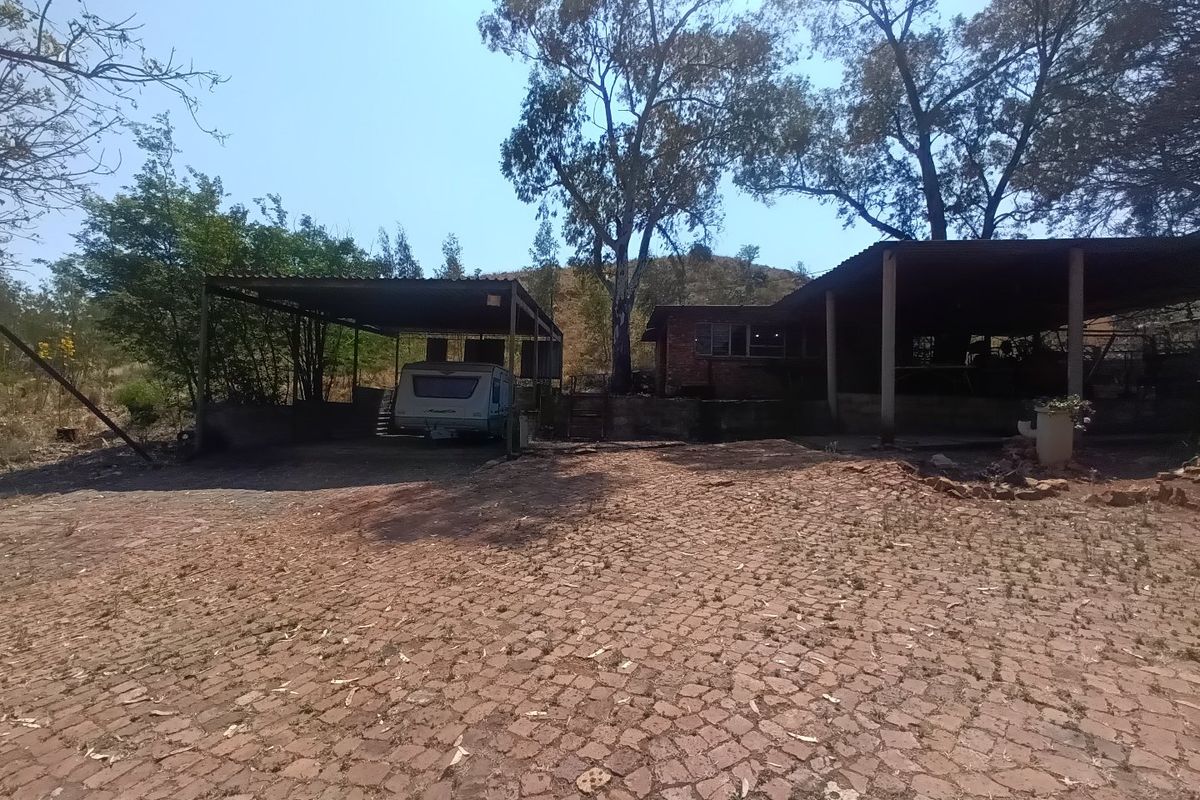 Rear exterior view of the farm property featuring a large paved area, covered carport structure, and brick building facade surrounded by mature trees.
