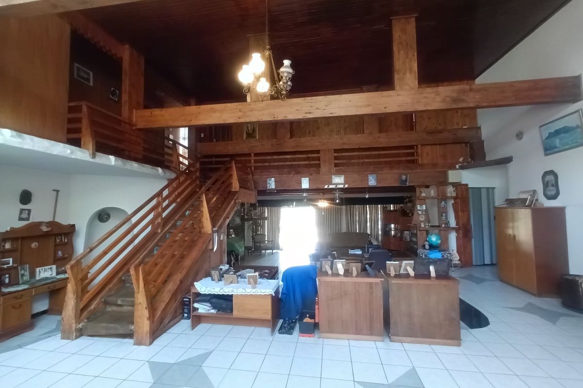 Spacious open-plan living area featuring a prominent timber staircase, mezzanine level, exposed wooden beams, and tiled flooring throughout.