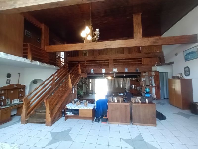 Spacious open-plan living area featuring a prominent timber staircase, mezzanine level, exposed wooden beams, and tiled flooring throughout.