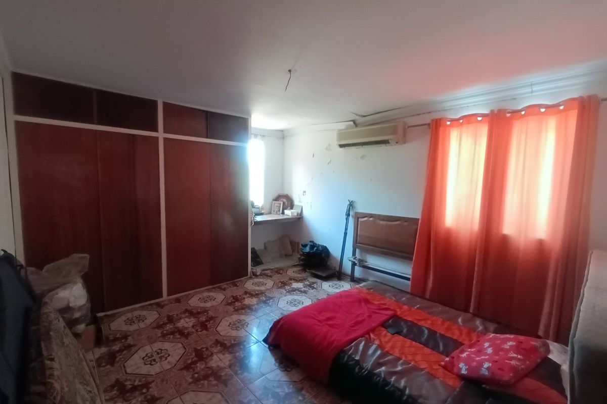 A bedroom featuring built-in wooden cupboards, tiled flooring, and a wall-mounted air conditioning unit, requiring cosmetic updates to the walls and ceiling.