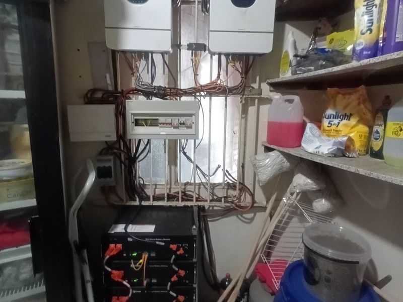 Utility space featuring a solar power system with dual inverters and a battery bank, alongside built-in storage shelving.