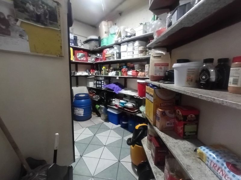 A functional scullery or pantry area featuring extensive built-in shelving and tiled flooring, providing ample storage space for household supplies.