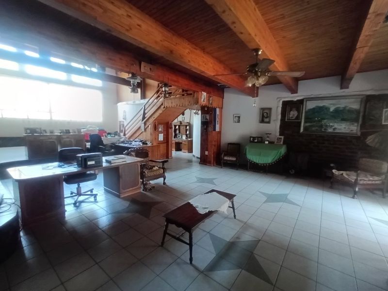 Spacious living area featuring exposed timber ceiling beams, a feature brick fireplace, and unique star-patterned tiled flooring with an integrated timber staircase.
