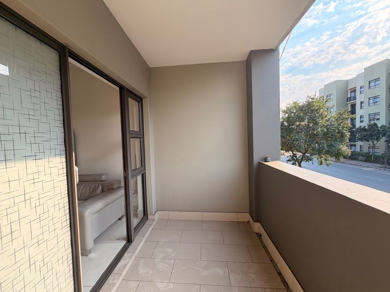 A clean, covered balcony featuring tiled flooring and a solid balustrade, offering a view of the surrounding apartment complex and street.