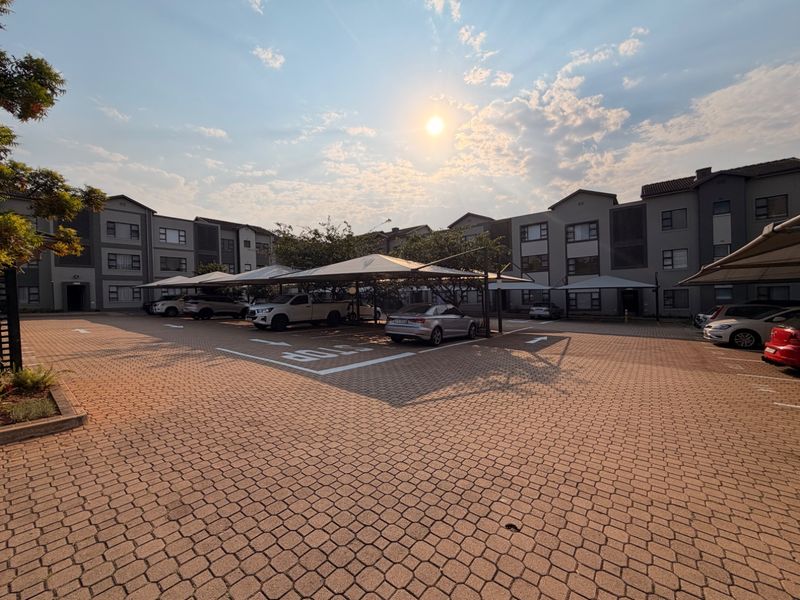 Exterior view of an apartment complex featuring a paved parking area with covered carports and multi-story residential building facades.