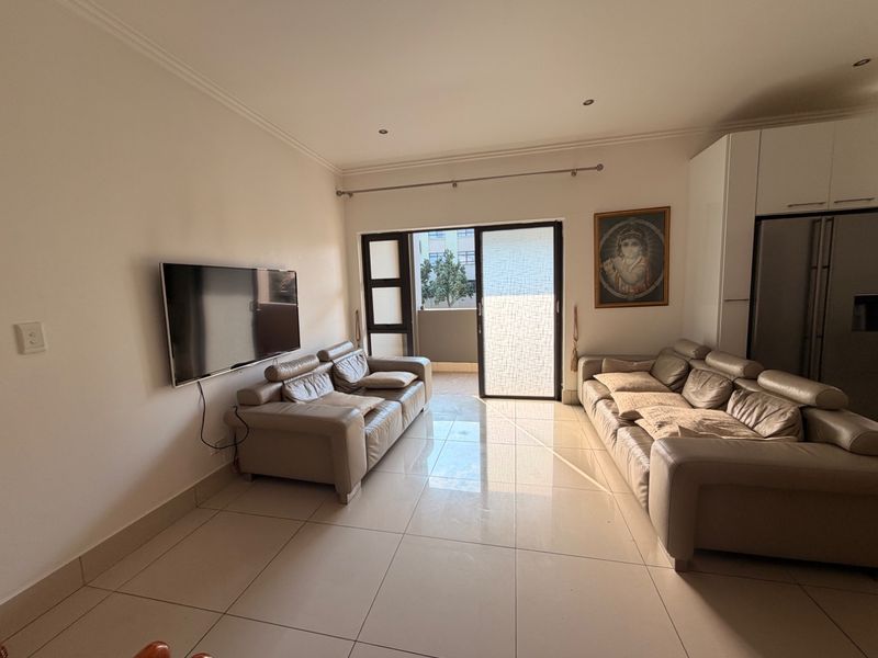 An open-plan living area featuring large floor tiles, recessed lighting, and a sliding glass door providing access to an outdoor balcony space.