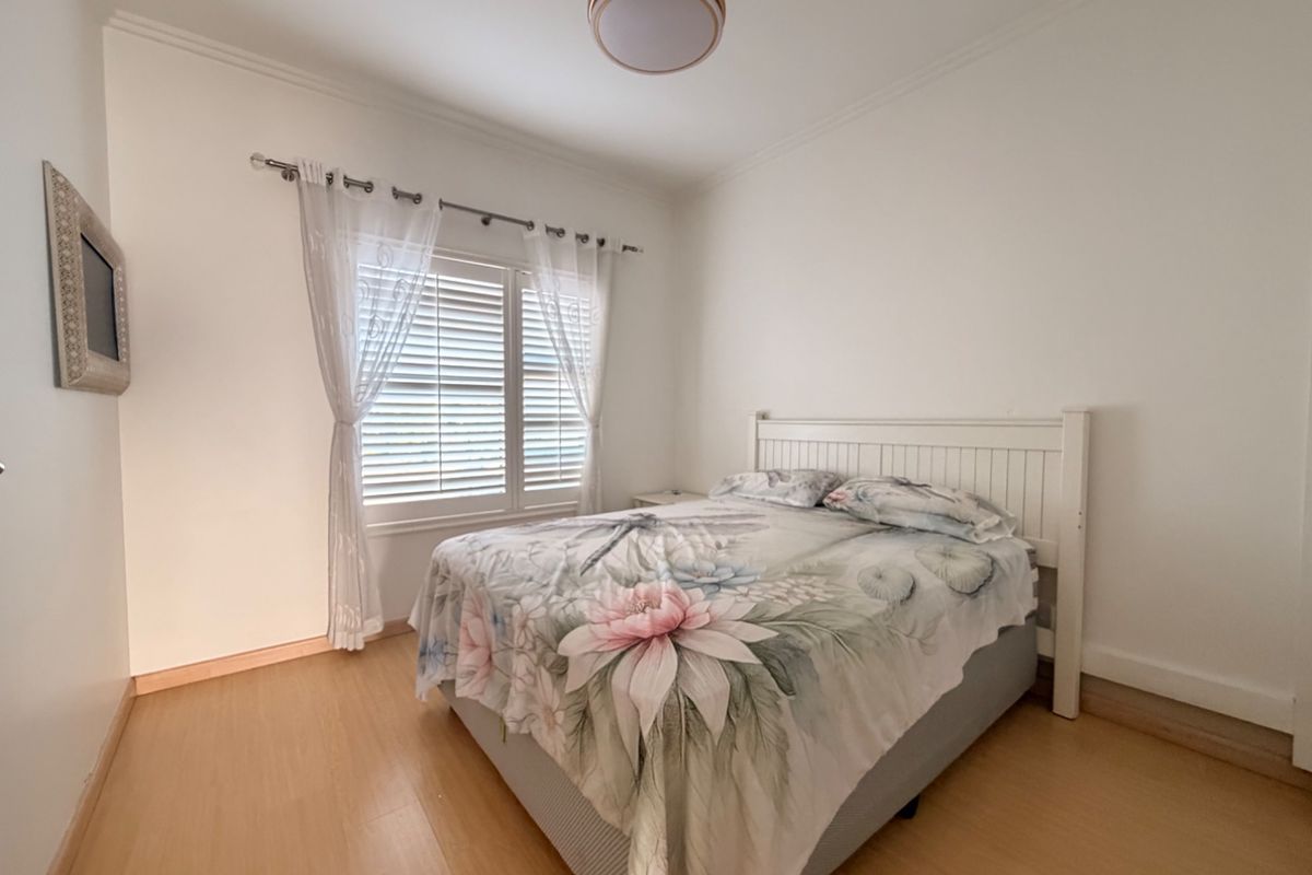 A bright and well-maintained bedroom featuring laminate flooring, crown molding, and window shutters, providing a clean and neutral space.