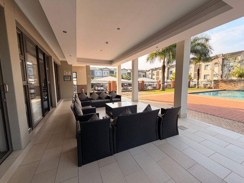 A spacious covered patio area featuring tiled flooring and recessed lighting, providing direct access to the pool area and complex grounds.