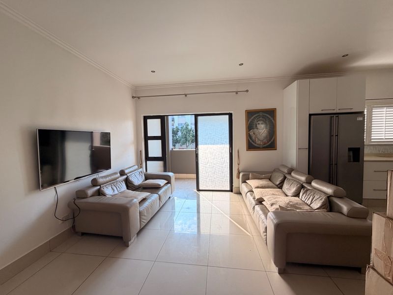 An open-plan living area featuring tiled flooring, recessed lighting, and direct access to a balcony through a sliding glass door.