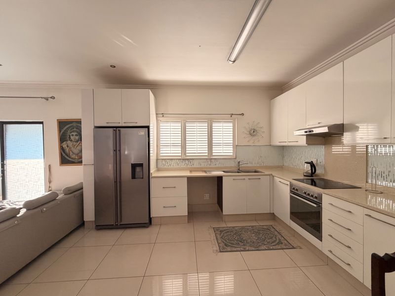 Modern open-plan kitchen featuring white high-gloss cabinetry, stone countertops, integrated appliances, and tiled flooring, seamlessly connected to the living area.