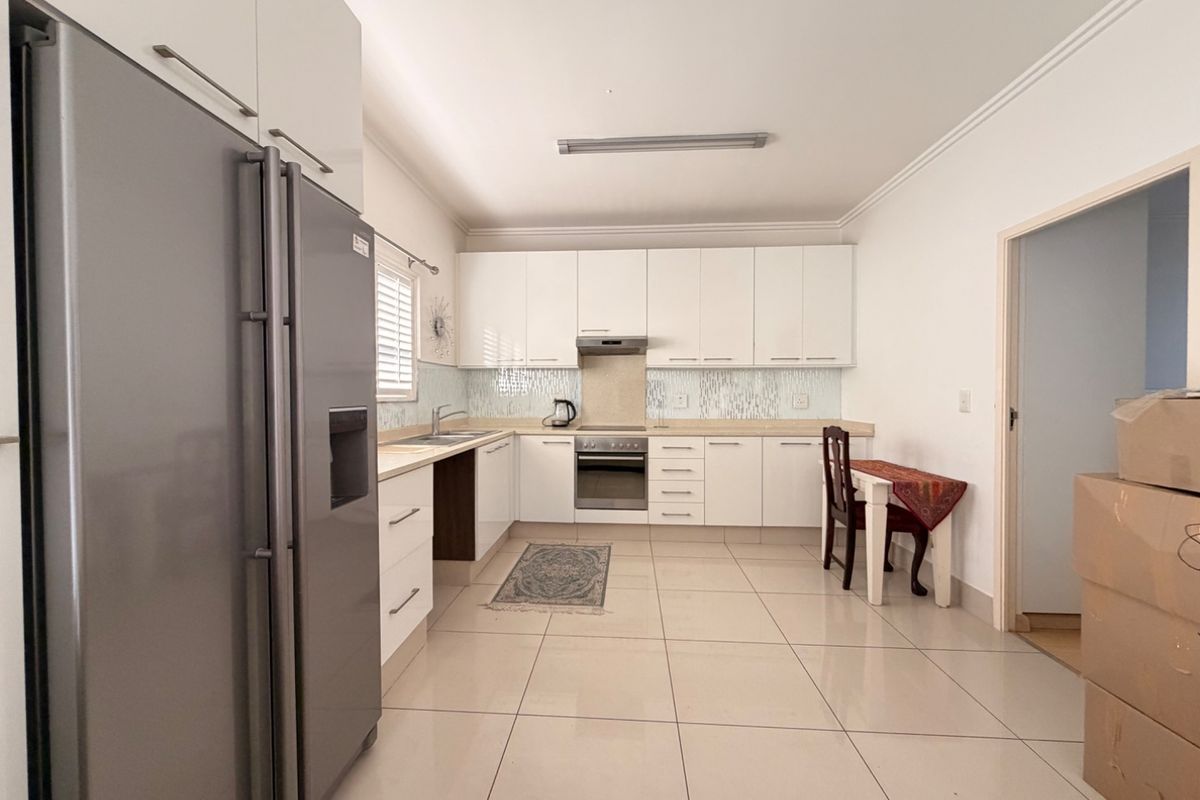 A clean, functional kitchen featuring white cabinetry, tiled backsplash, stainless steel oven, extractor fan, and neutral ceramic floor tiles.