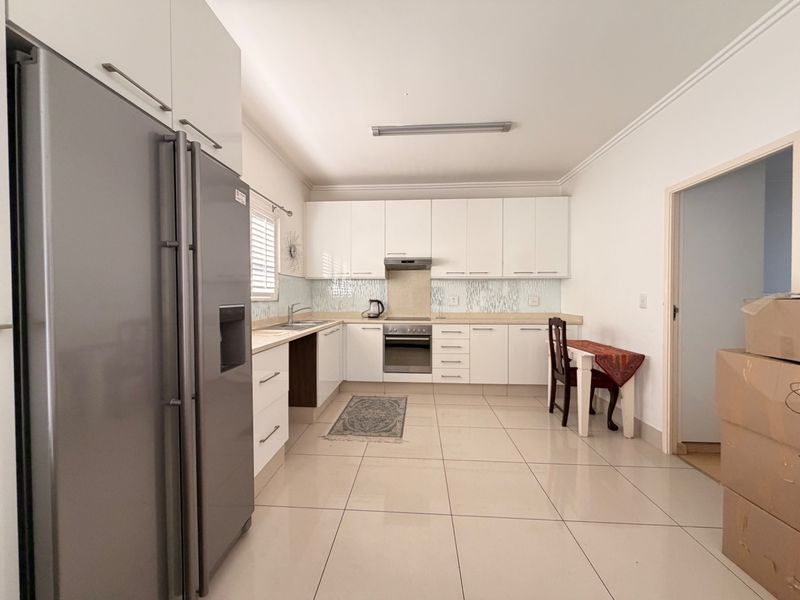 A clean, functional kitchen featuring white cabinetry, tiled backsplash, stainless steel oven, extractor fan, and neutral ceramic floor tiles.