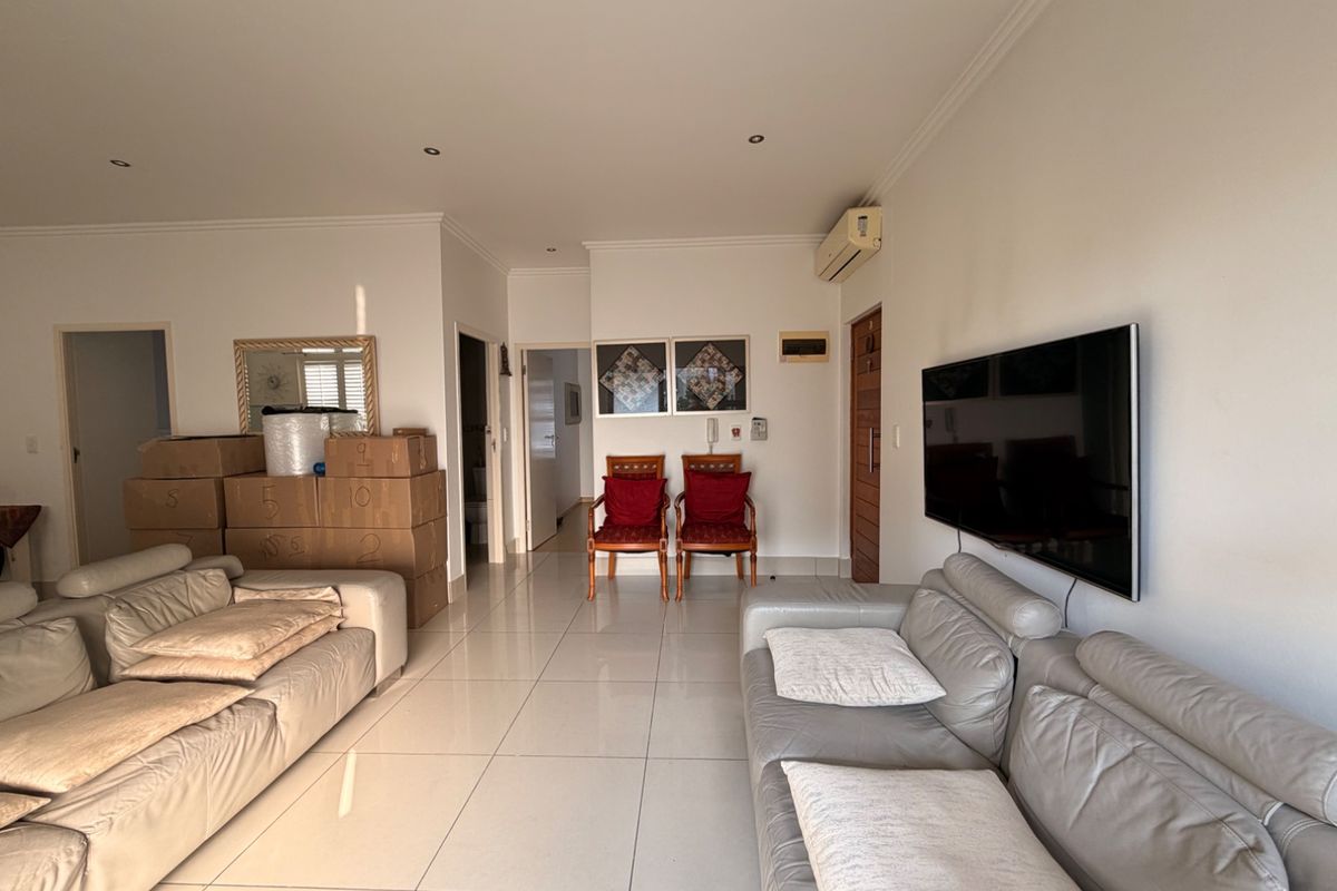 Spacious living area featuring neutral tiled flooring, recessed downlighting, and a wall-mounted air conditioning unit.