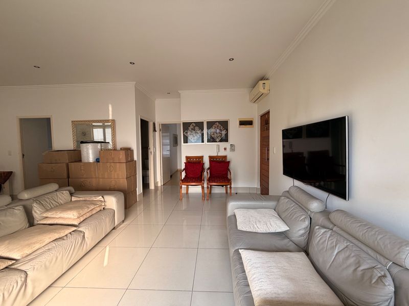 Spacious living area featuring neutral tiled flooring, recessed downlighting, and a wall-mounted air conditioning unit.