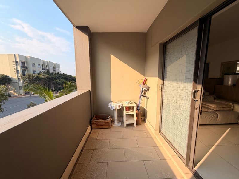 A covered balcony featuring tiled flooring and a sliding glass door, offering an outdoor space with views of the surrounding complex.