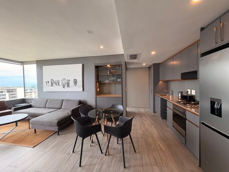 Modern open-plan apartment featuring a sleek kitchen with integrated appliances, wood-look flooring, and a spacious living area with floor-to-ceiling windows.