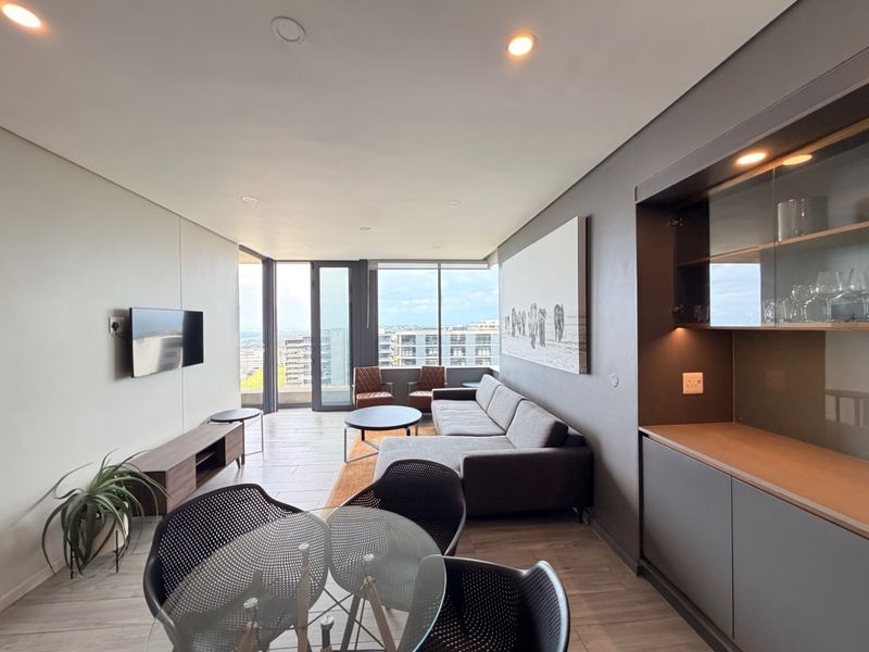 Modern open-plan living area featuring sleek built-in cabinetry, recessed lighting, and large sliding glass doors leading to a balcony with city views.