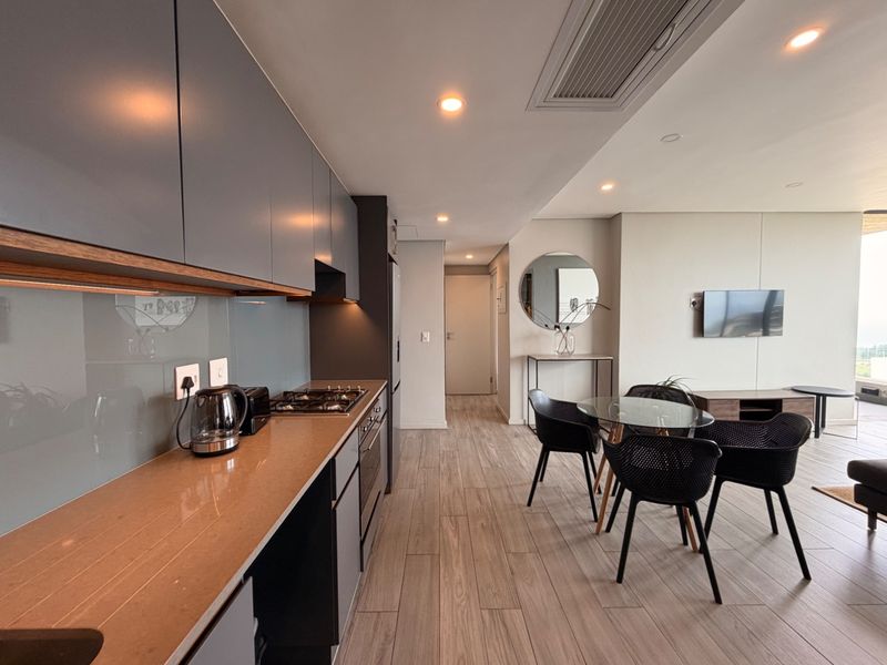 Modern open-plan kitchen and living area featuring sleek grey cabinetry, stone countertops, integrated appliances, and wood-look tile flooring with ducted air conditioning.