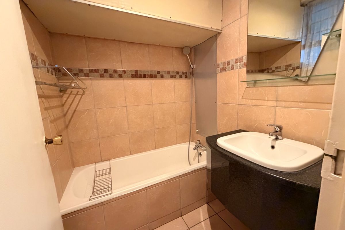 A functional bathroom featuring a bathtub with shower attachment, a vanity basin with granite countertop, and neutral wall tiling.