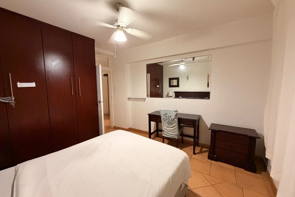 A bedroom featuring built-in wooden cupboards, a ceiling fan, and tiled flooring, offering a functional and well-maintained living space.