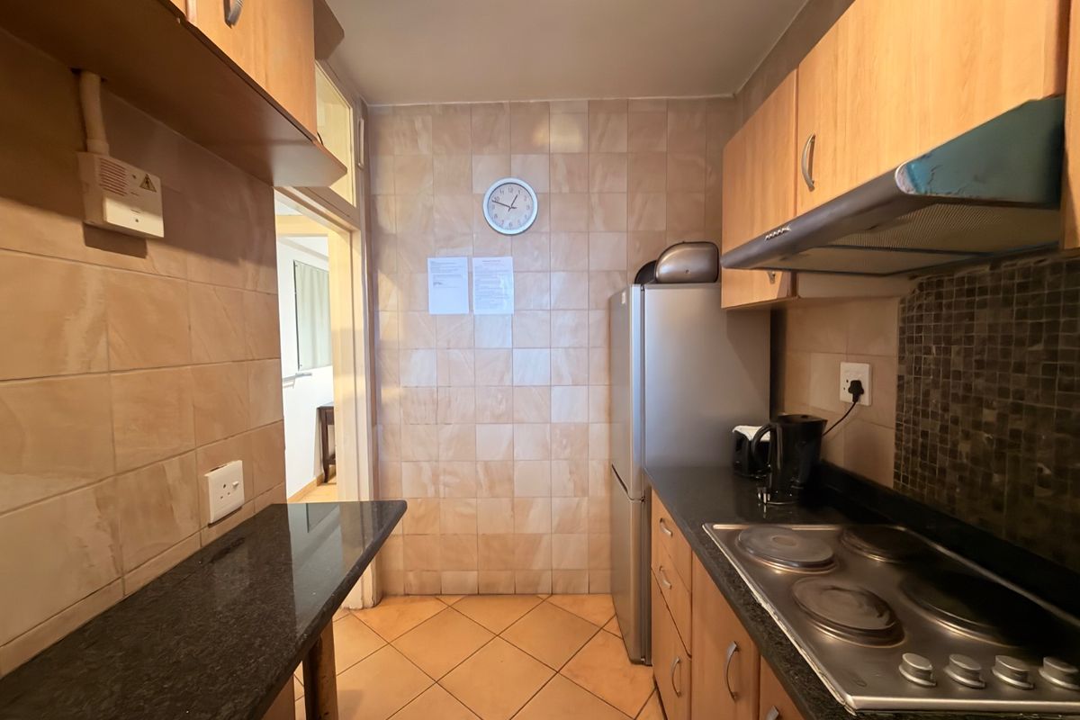 A compact kitchen featuring wooden cabinetry, granite countertops, an electric hob with extractor fan, and tiled finishes throughout.