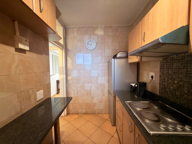 A compact kitchen featuring wooden cabinetry, granite countertops, an electric hob with extractor fan, and tiled finishes throughout.