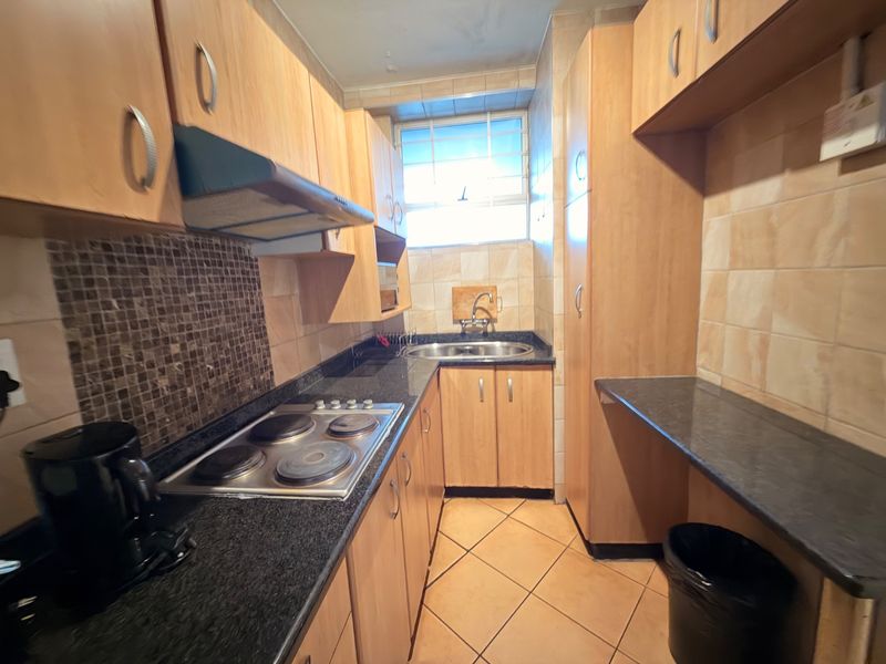 Compact kitchen featuring wooden cabinetry, granite countertops, an integrated electric hob with extractor fan, and tiled finishes throughout.