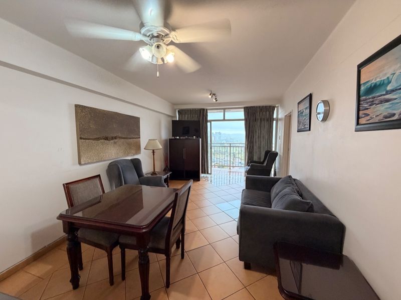 An open-plan living and dining area featuring tiled flooring, a ceiling fan, and direct access to a balcony with exterior views.