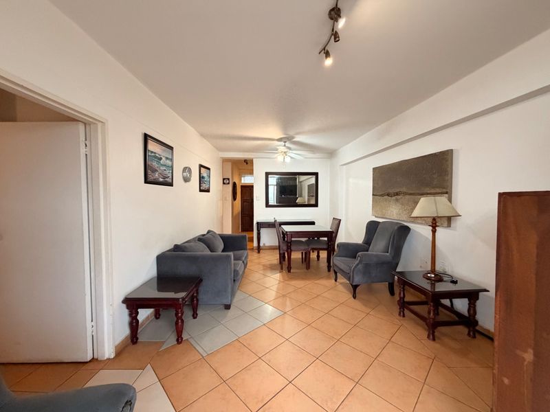 A spacious living and dining area featuring ceramic tile flooring, a ceiling fan, and track lighting, offering a functional layout for relaxation and meals.