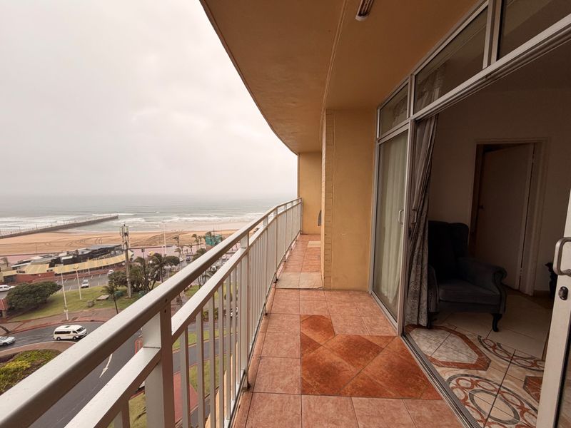 A spacious balcony featuring tiled flooring and a metal balustrade, offering direct access to the interior and expansive coastal views.