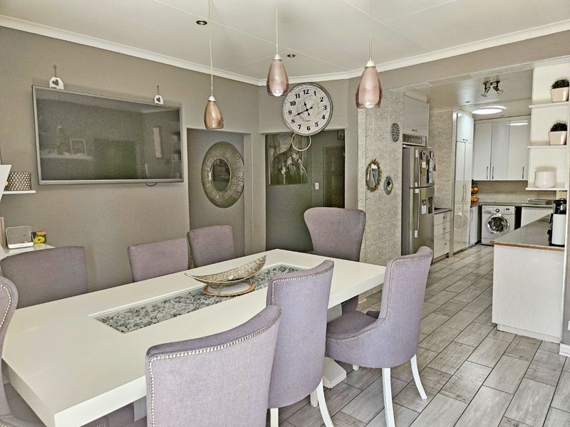 Open plan dining area flowing into a functional kitchen with tiled flooring, modern pendant lighting, and integrated laundry facilities.