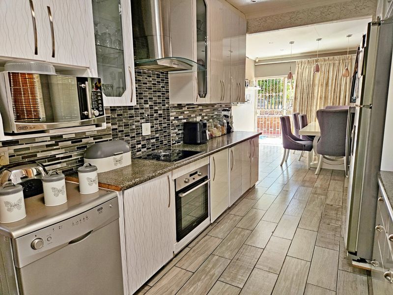 Modern open-plan kitchen featuring sleek cabinetry, mosaic tile backsplash, stone countertops, and integrated appliances, flowing seamlessly into the adjacent dining area.