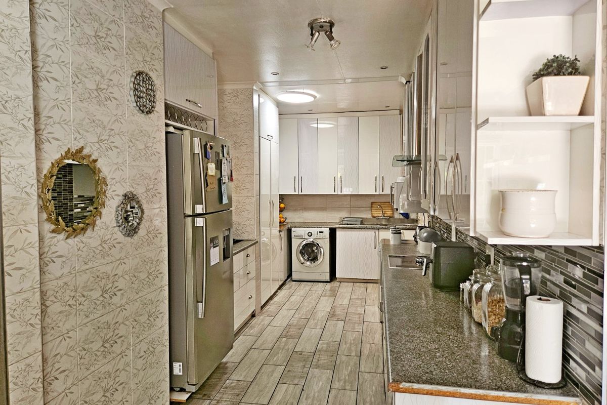 A functional galley-style kitchen featuring modern white cabinetry, granite countertops, tiled flooring, and integrated laundry appliances.