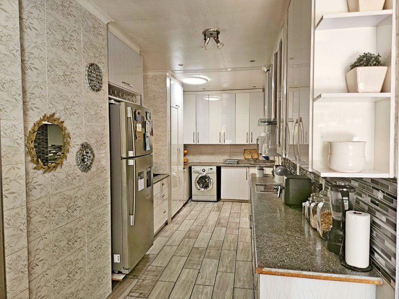 A functional galley-style kitchen featuring modern white cabinetry, granite countertops, tiled flooring, and integrated laundry appliances.