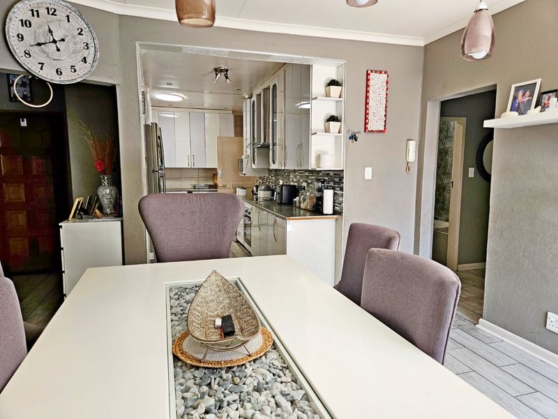Open plan dining area flowing into a functional kitchen with modern cabinetry and tiled backsplash, creating a cohesive living space.
