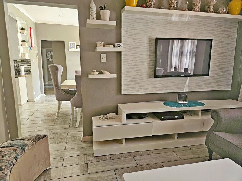 Open plan living area featuring a modern built-in media wall with floating shelves and tiled flooring, leading through to the dining and kitchen space.