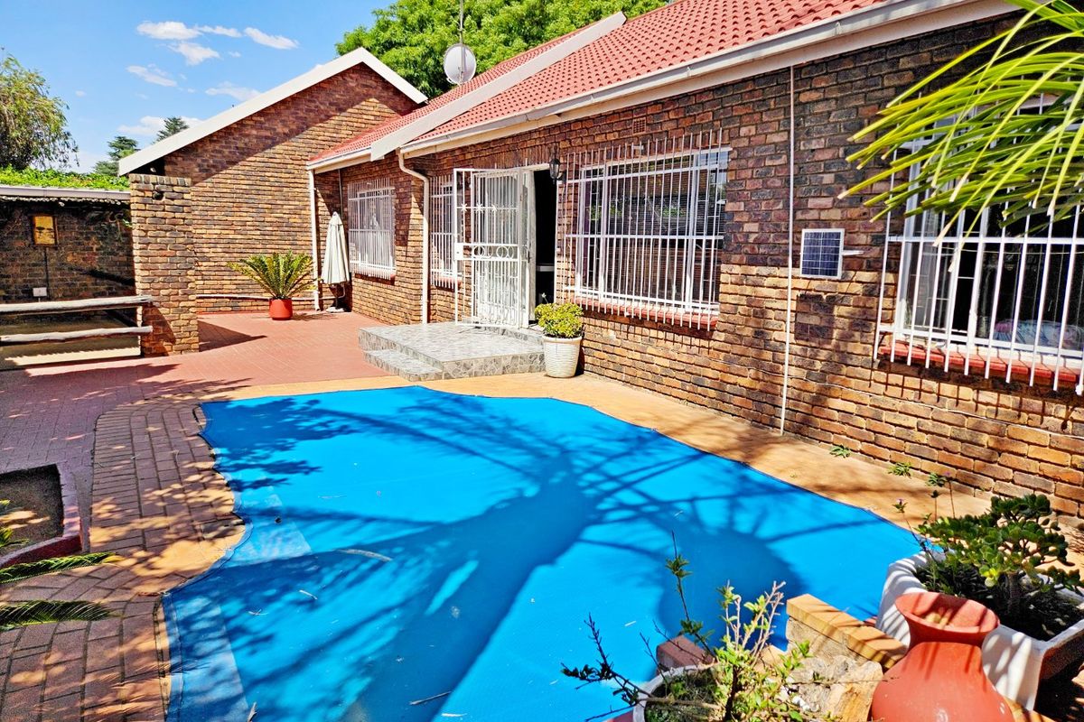Rear exterior view of a face brick townhouse featuring a swimming pool with a cover, paved patio area, and secure window bars.