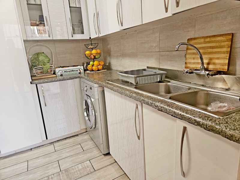A functional kitchen featuring white cabinetry, granite countertops, a double stainless steel sink, and integrated laundry facilities with modern tiled finishes.