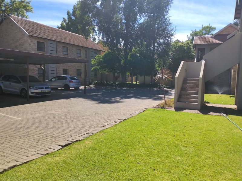 Exterior view of an apartment complex featuring a paved driveway, covered parking bays, and a communal lawn area with concrete stair access.