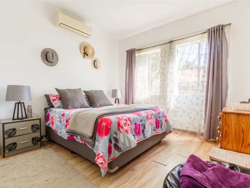 A well-lit bedroom featuring laminate flooring, a wall-mounted split-system air conditioner, and large windows allowing for natural light.