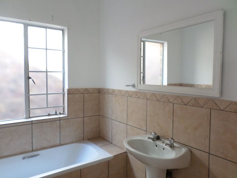 A functional bathroom featuring a pedestal basin, built-in bathtub, and tiled wall finishes, offering a clean space ready for potential cosmetic updates.