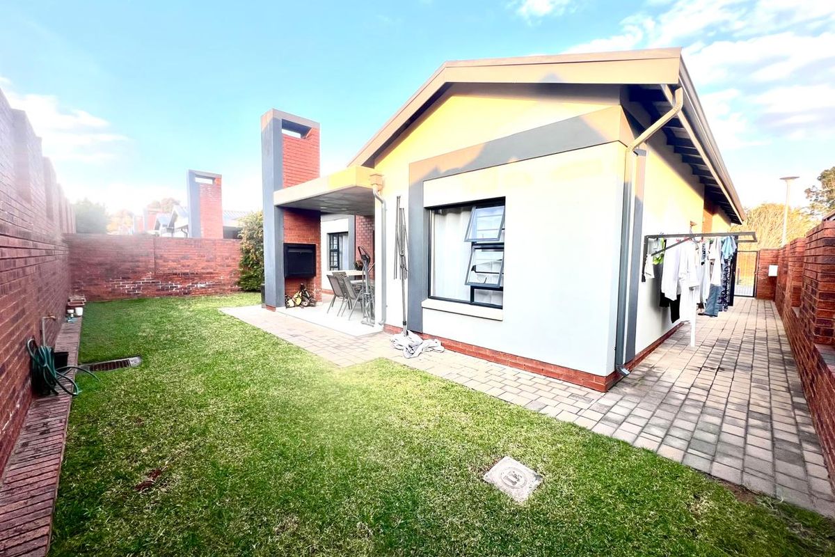 Rear view of the property featuring a paved patio with a built-in braai, a small lawn, and brick boundary walls.