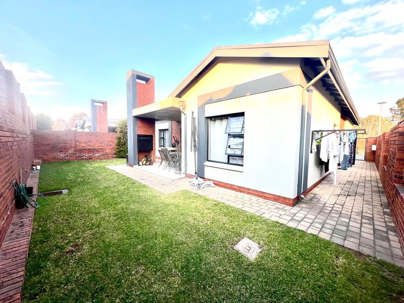 Rear view of the property featuring a paved patio with a built-in braai, a small lawn, and brick boundary walls.