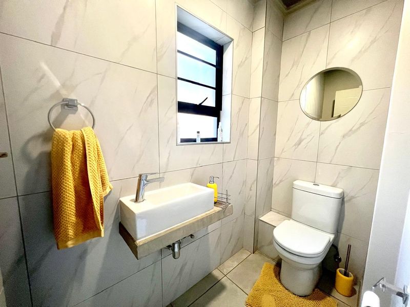 A modern, compact bathroom featuring marble-look wall tiles, a wall-mounted basin, and a standard toilet.