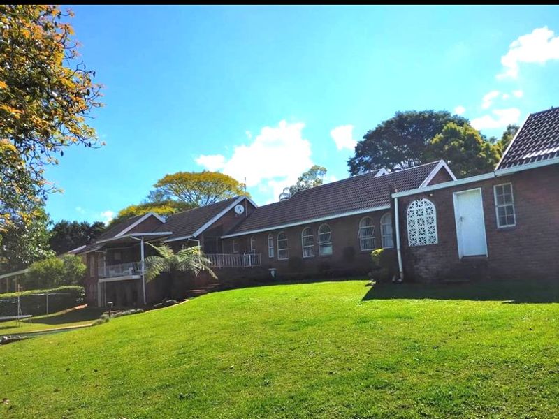 Rear view of a brick house featuring a tiled roof, balcony with railing, and a spacious lawn area.