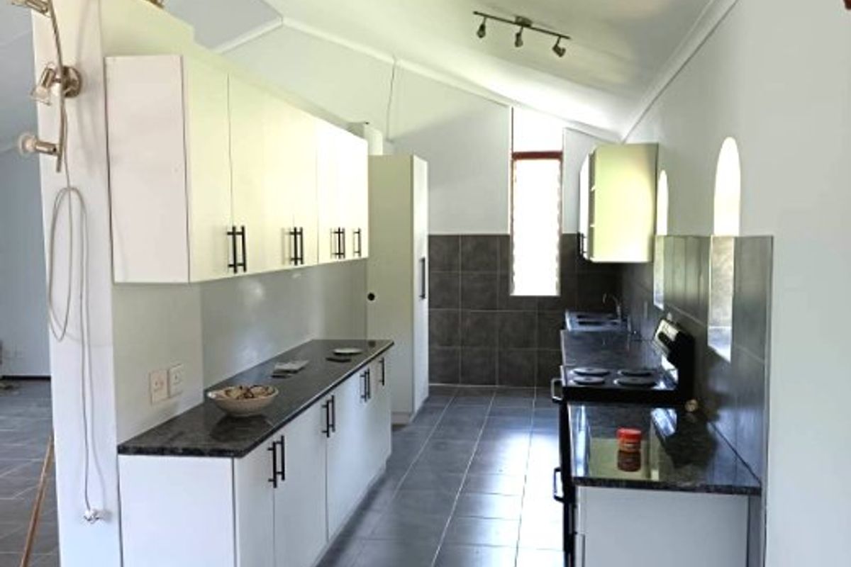 A clean, functional kitchen featuring white cabinetry, dark granite countertops, tiled flooring, and a vaulted ceiling with track lighting.